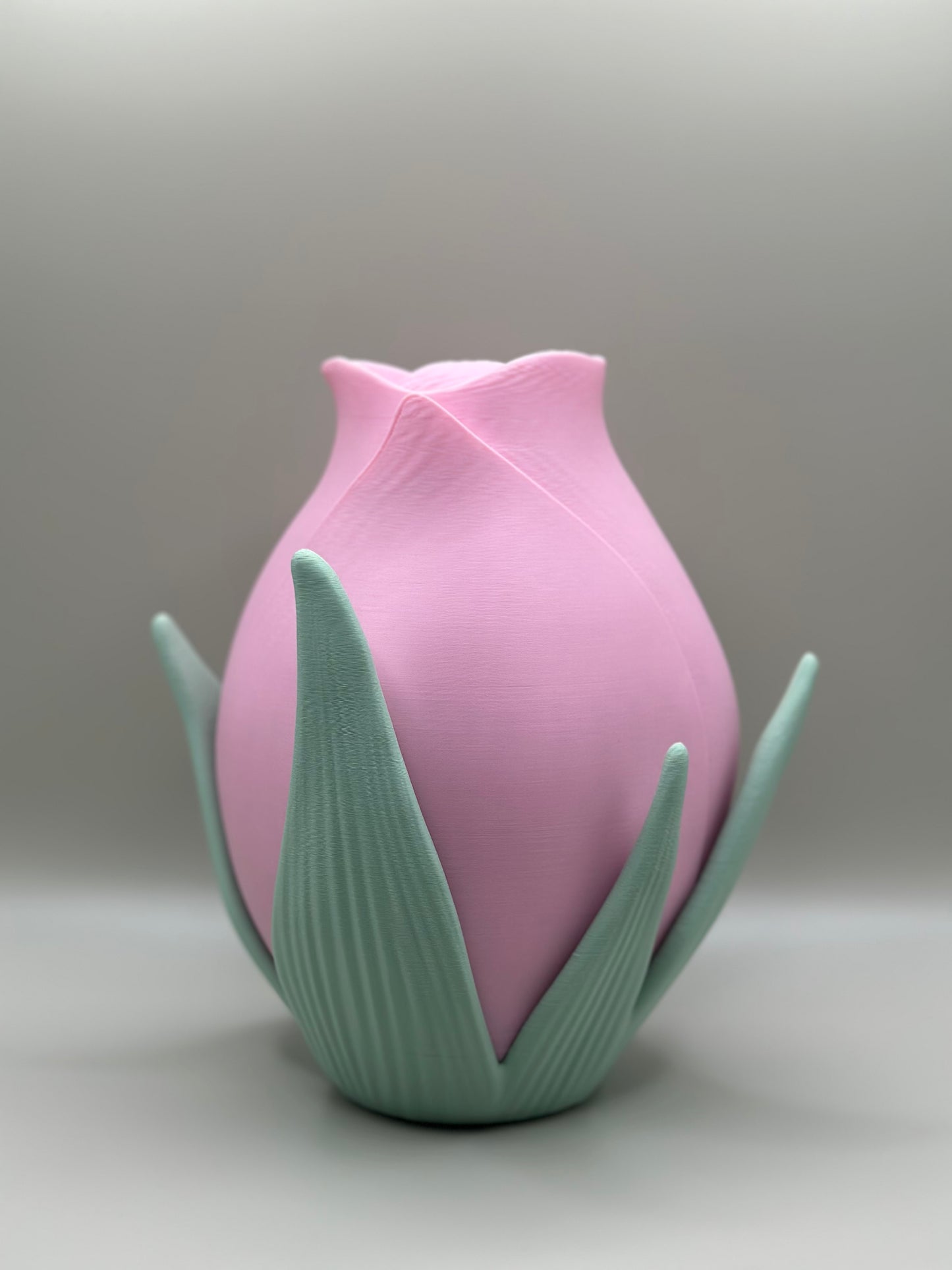 3D printed pink vase shaped like a rose with green sculpted leaves